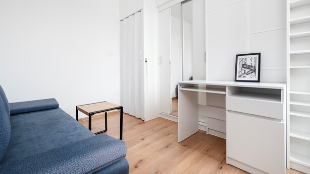 Ett rum med en blå soffa, ett litet bord, ett vitt skrivbord och en vit garderob.