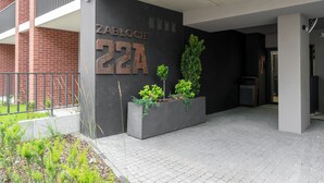 Ein Gebäudeeingang mit einer schwarzen Wand, einem Metallschild mit der Aufschrift 'ZABLOCIE 22A' und einem Pflanzgefäß mit Pflanzen.