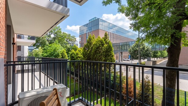 Ein Balkon mit Blick auf ein modernes Gebäude, ein Holzstuhl und eine Klimaanlage.