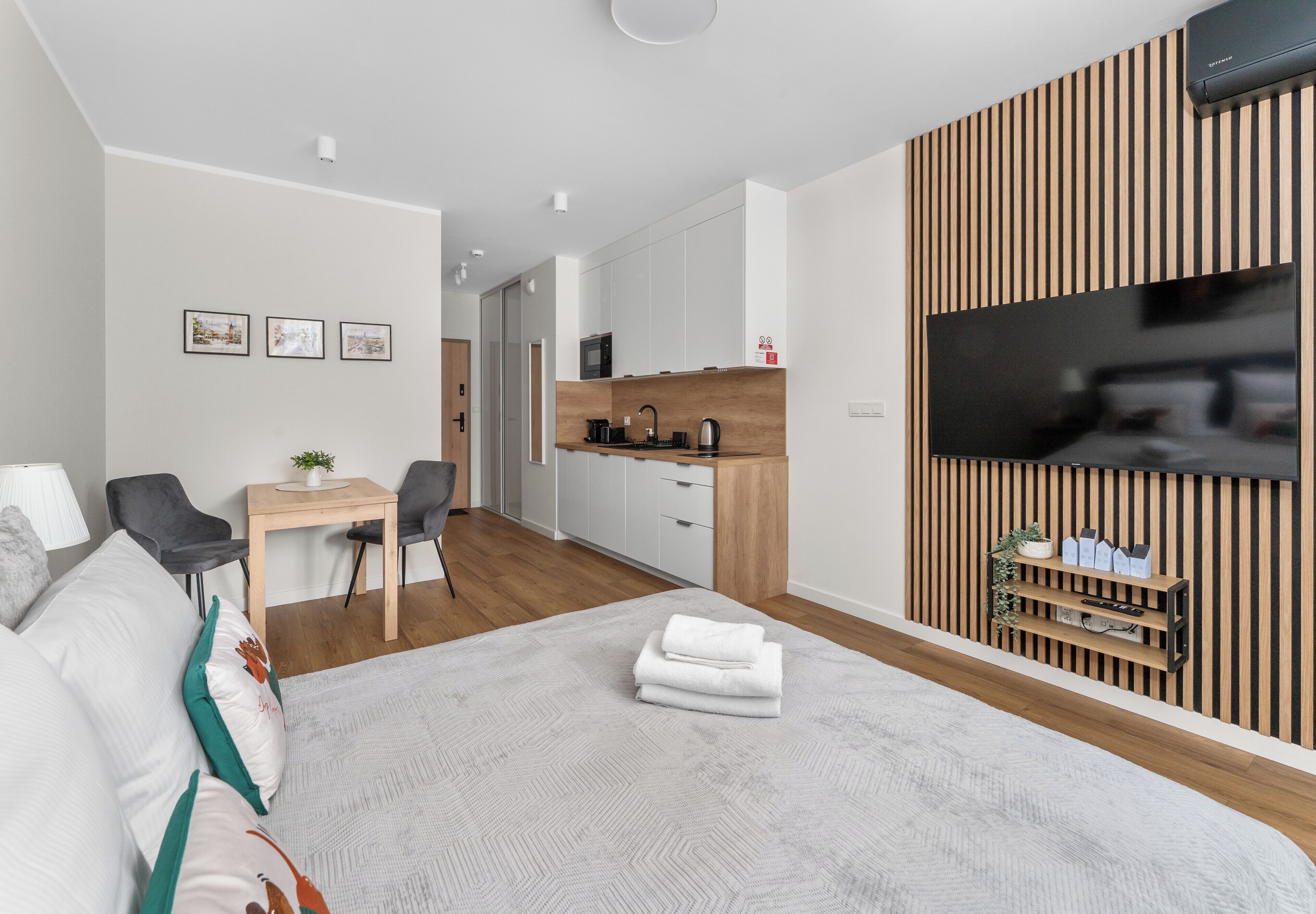 Ein modernes Hotelzimmer mit Bett, Schreibtisch, Stuhl, einer Küchenzeile und einem an der Wand montierten Fernseher.