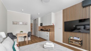 Ein modernes Hotelzimmer mit Bett, Schreibtisch, Stuhl, einer Küchenzeile und einem an der Wand montierten Fernseher.