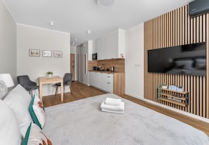 Ein modernes Hotelzimmer mit Bett, Schreibtisch, Stuhl, einer Küchenzeile und einem an der Wand montierten Fernseher.