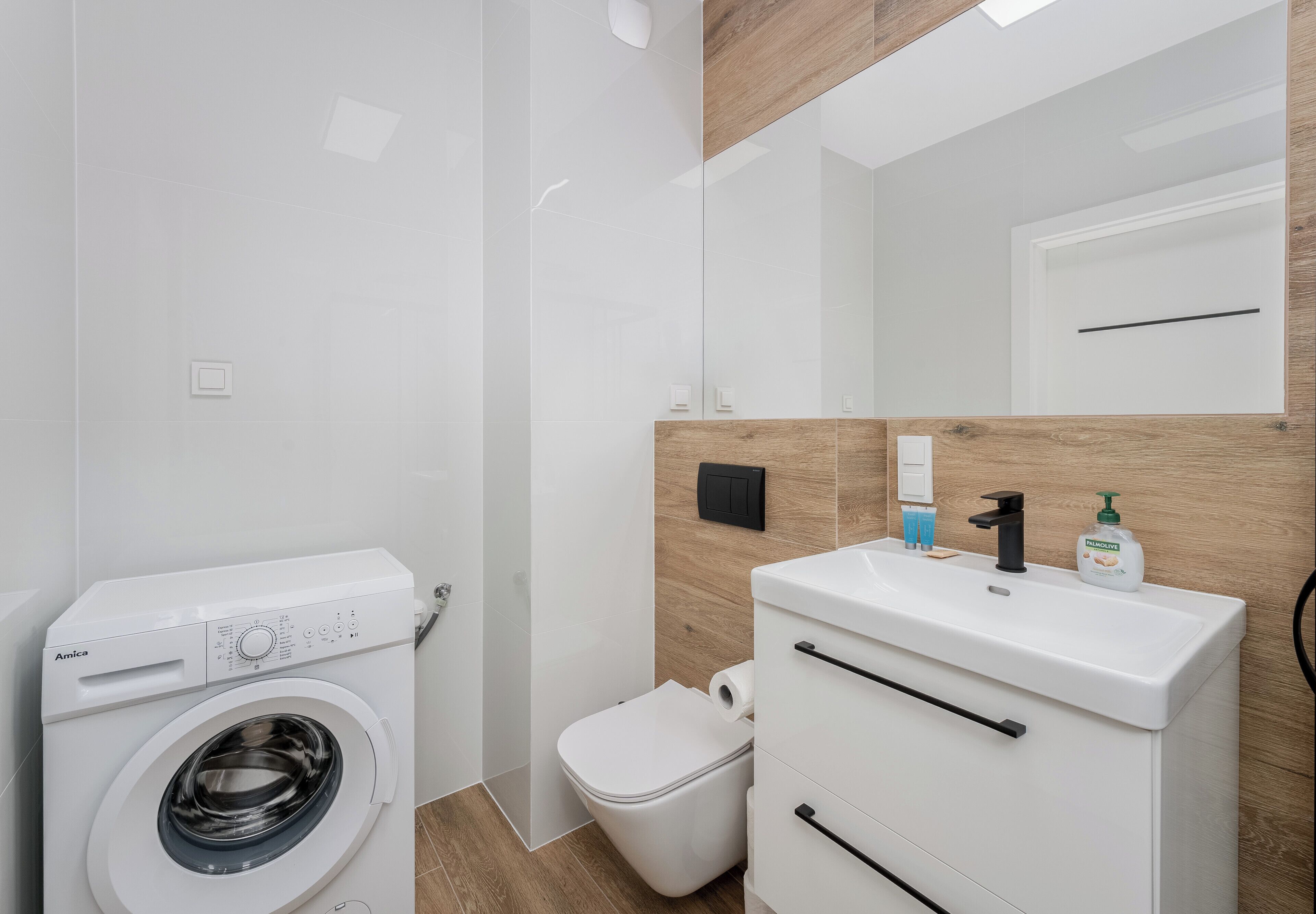 Un baño moderno con lavadora, inodoro y muebles blancos.