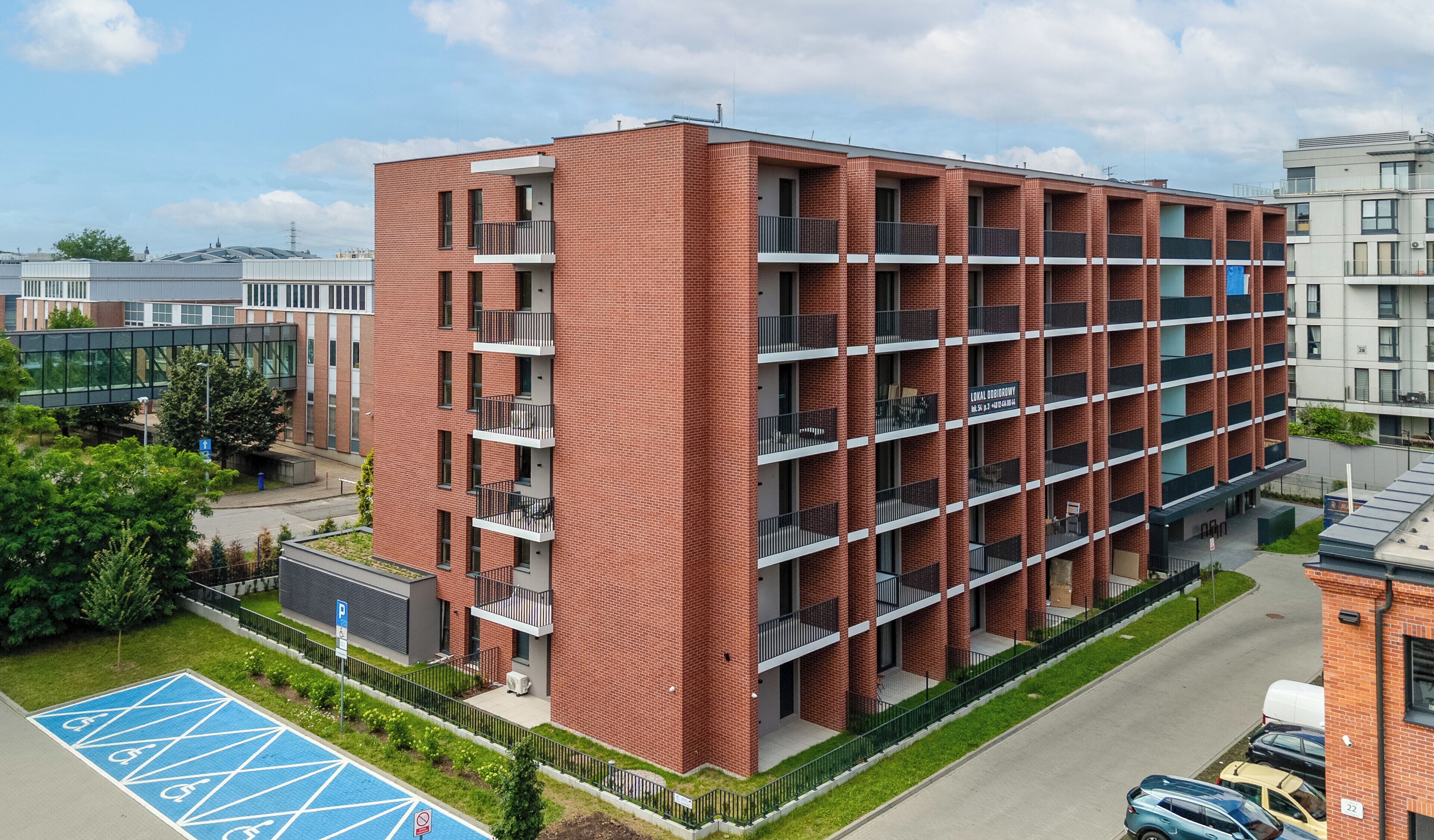 A multi-story brick building with balconies, a parking area, and a sports court.