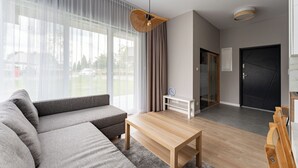 A modern living room with a sofa, a wooden coffee table, a hanging light fixture, a white side table, and a black door. - Willa 28D Lakeside Retreat Łączyno (Łączyno)