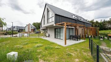 A modern house with a large patio, surrounded by a fenced garden with wildflowers.