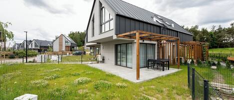 Una casa moderna con un patio amplio, rodeada por un jardín cercado con flores silvestres.