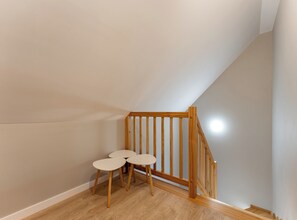 Una stanza con una scala in legno, un tavolino e tre sedie, e un soffitto a falde.