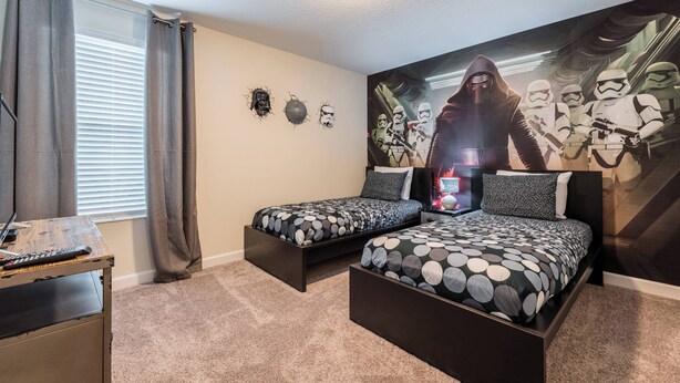 Een slaapkamer met twee bedden, een bureau en muurdecoratie met Star Wars thema.