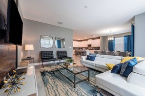 Een moderne woonkamer met een bank, twee fauteuils, een salontafel en een televisie.
