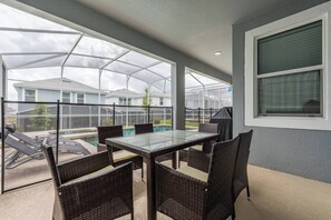 An outdoor patio with a glass table and wicker chairs, overlooking a swimming pool and neighboring houses. - Luxury 6BR Home with Private Pool (Davenport)
