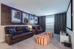 A modern living room with a brown leather sofa, striped ottomans, and framed movie posters on the wall. - Luxury 6BR Home with Private Pool (Davenport)