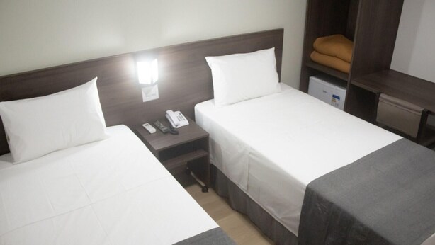 Ein Hotelzimmer mit zwei Einzelbetten, einem Nachttisch mit Telefon und Lampe sowie einem kleinen Schreibtisch mit Stuhl.