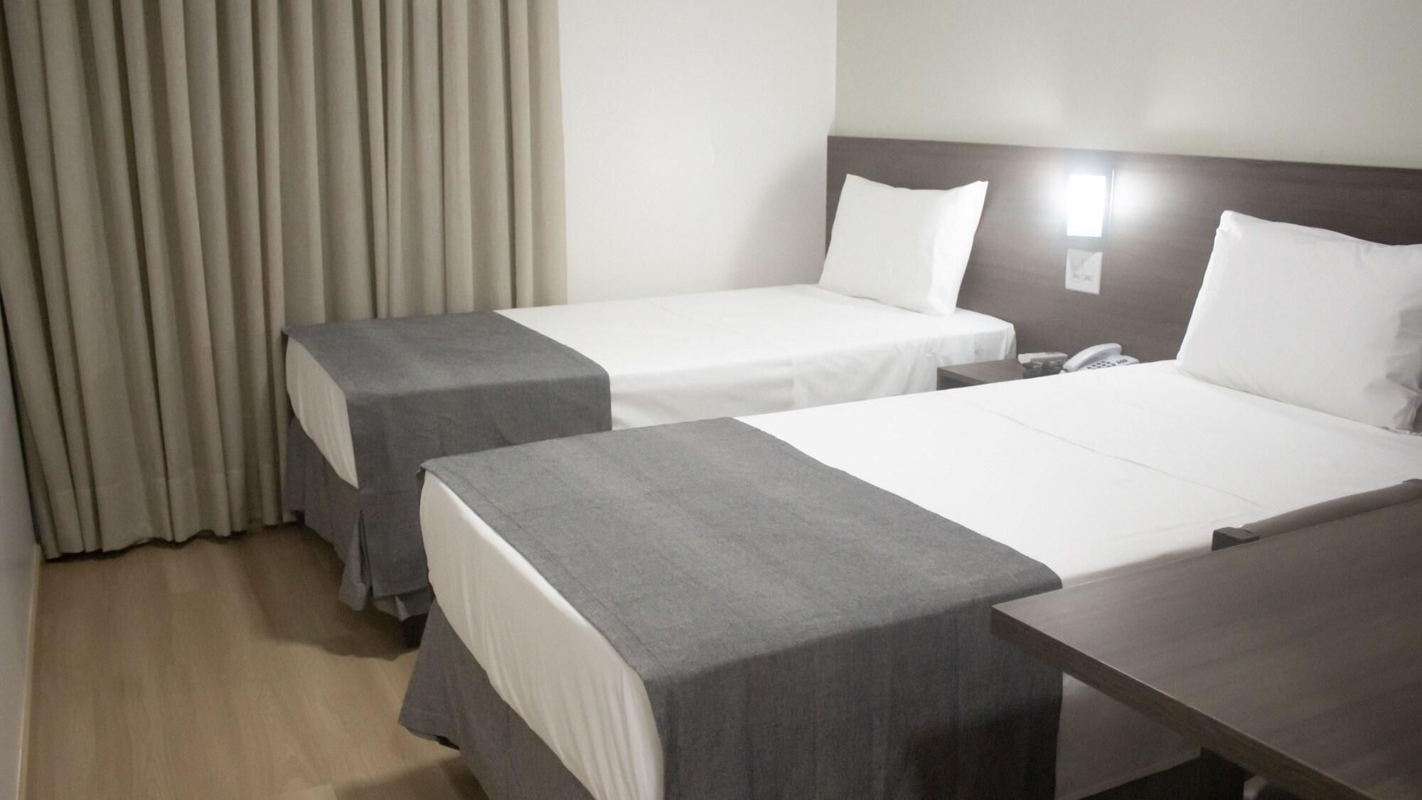 Quarto de hotel com duas camas, mesa de cabeceira e telefone.