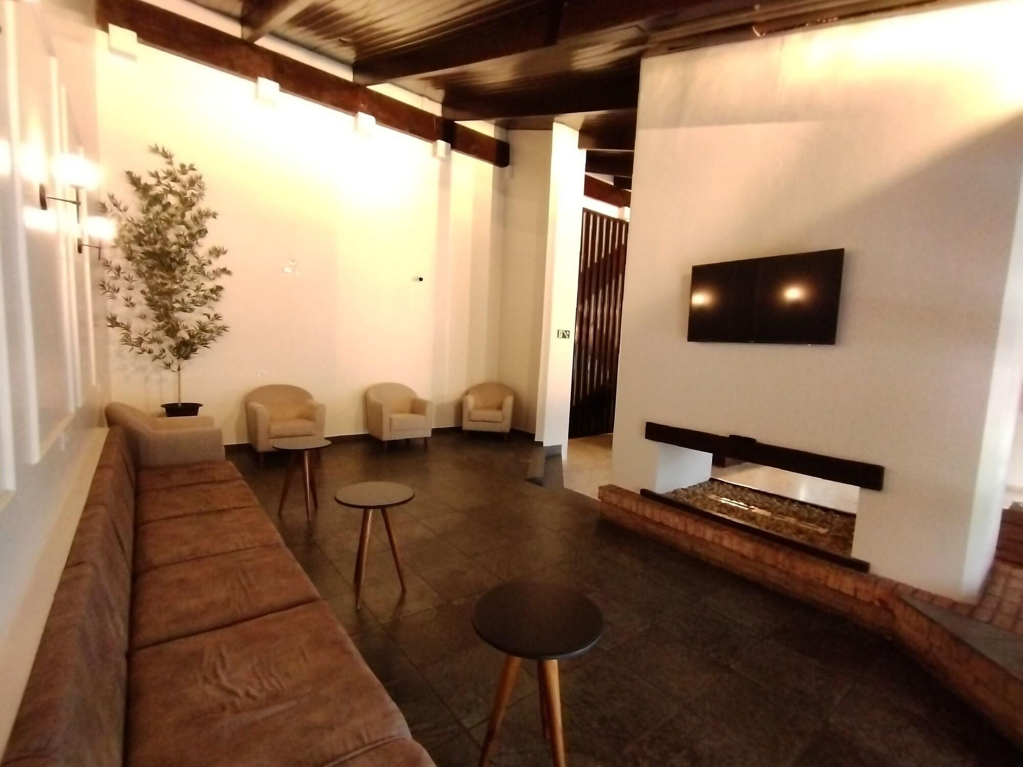 Uma sala de estar moderna com um sofá marrom, duas poltronas, uma mesa redonda pequena, uma TV de tela plana na parede e uma lareira.