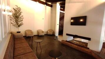 Uma sala de estar moderna com um sofá marrom, duas poltronas, uma mesa redonda pequena, uma TV de tela plana na parede e uma lareira.