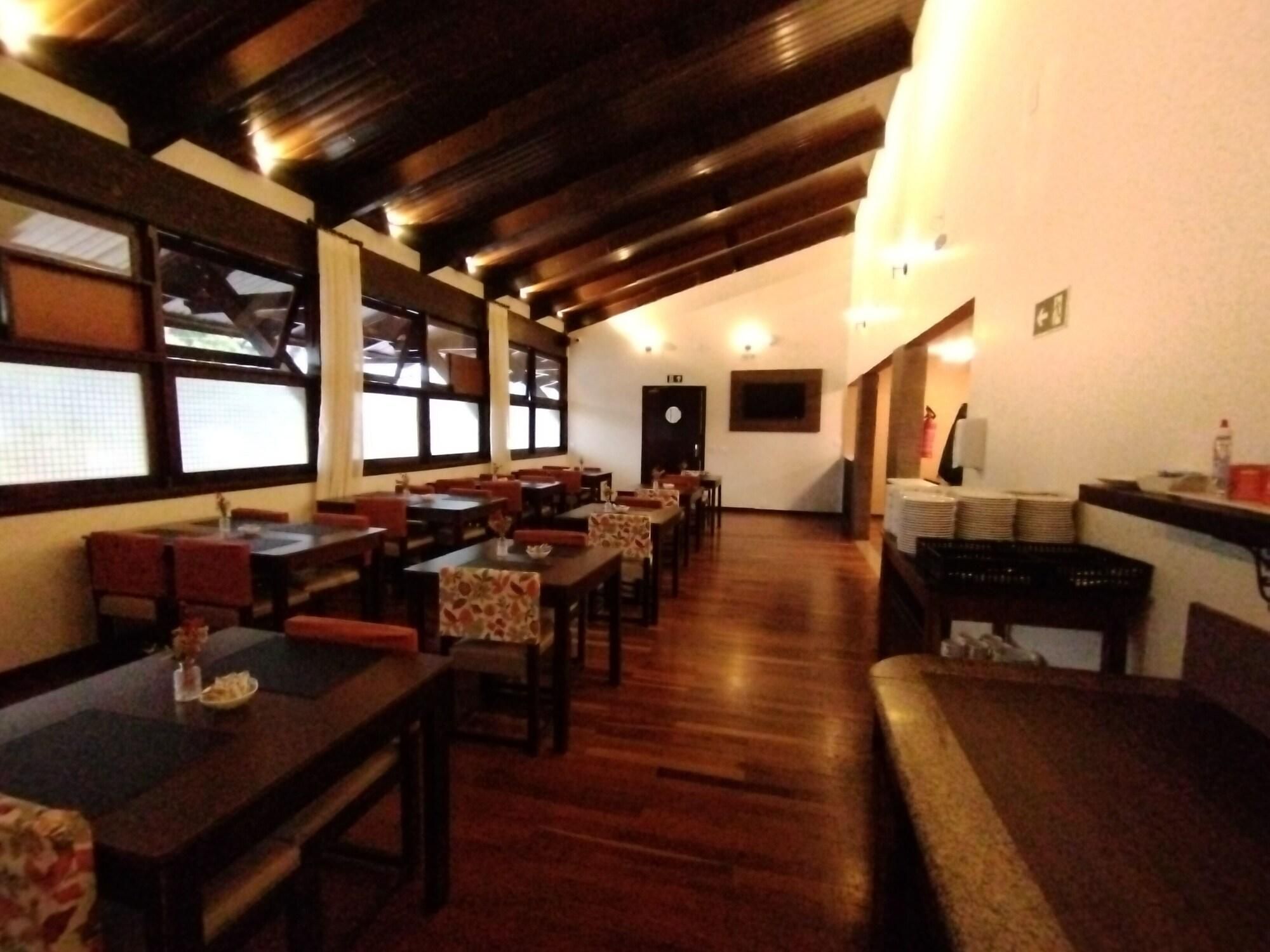 Um restaurante com mesas e cadeiras de madeira, um balcão com pratos empilhados e uma porta ao fundo.