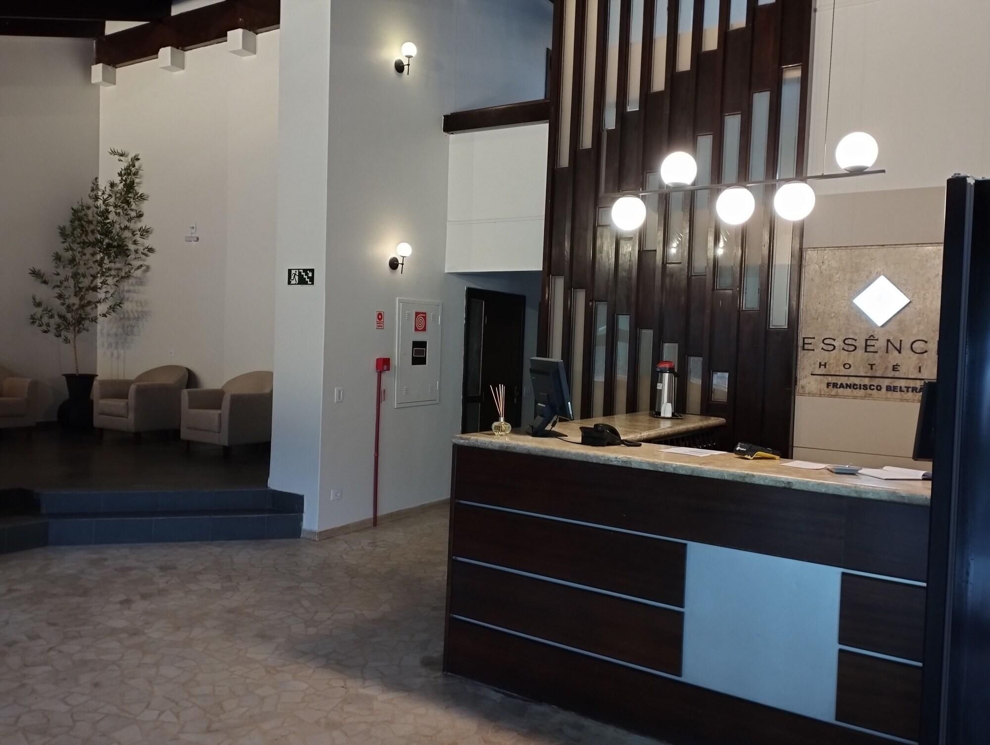 Uma receção de hotel com design moderno, uma planta em vaso e uma placa com o nome do hotel.