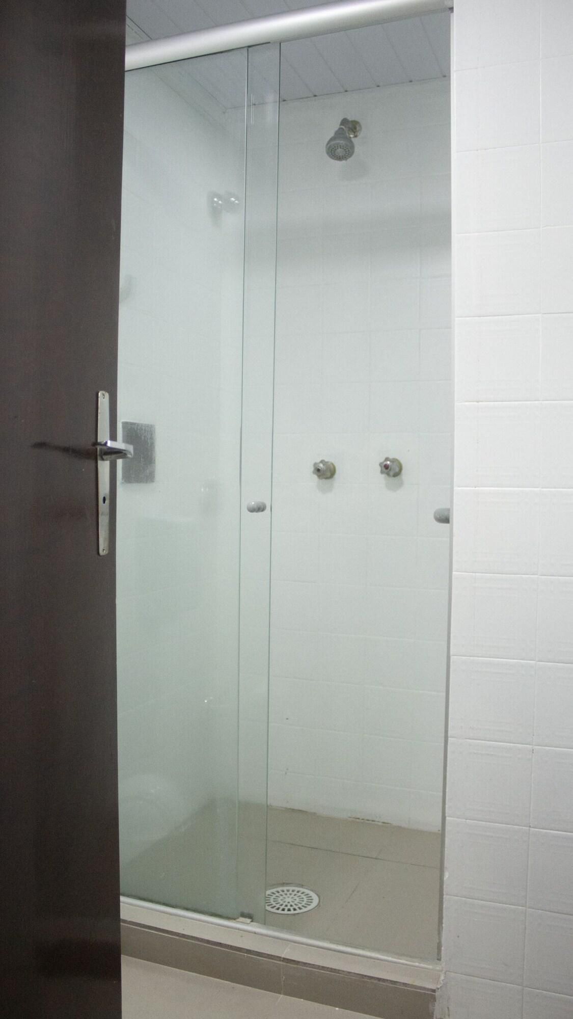 A glass-enclosed shower stall with a door handle, a showerhead, and a drain.