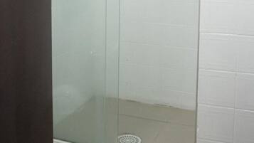A glass-enclosed shower stall with a door handle, a showerhead, and a drain.