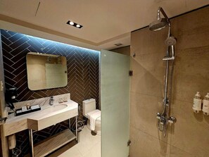 A modern bathroom with a herringbone-patterned wall, a large mirror, a white sink, a toilet, and a shower with a handheld showerhead.