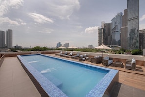 A rooftop swimming pool with lounge chairs and umbrellas, surrounded by high-rise buildings. - The Belamy House (Makati)