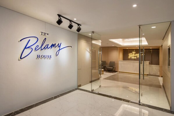 A hotel lobby with a reception desk, seating area, and a wall with the hotel's name. - The Belamy House (Makati)