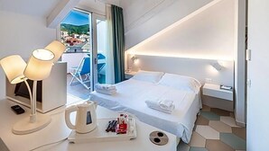 A hotel room with a bed, bedside table, lamp, and a view of the city. - Hotel Melograno (Spotorno)