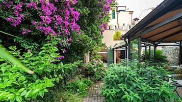 Un vialetto alberato conduce a un'area salotto all'aperto coperta, circondata da vegetazione rigogliosa e piante fiorite.