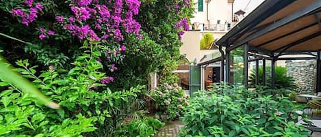 A garden path leading to a covered outdoor seating area with lush greenery and flowering plants.