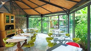 A covered outdoor dining area with tables and chairs, surrounded by glass walls and a stone wall. - Hotel Melograno (Spotorno)