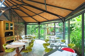 A covered outdoor dining area with tables and chairs, surrounded by glass walls and a stone wall. - Hotel Melograno (Spotorno)
