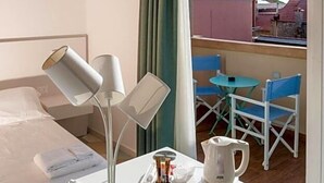 A hotel room with a bed, bedside lamps, a table with a kettle, and a view of the outside balcony. - Hotel Melograno (Spotorno)
