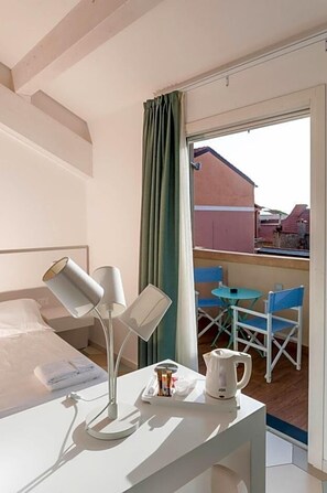 A hotel room with a bed, bedside lamps, a table with a kettle, and a view of the outside balcony. - Hotel Melograno (Spotorno)