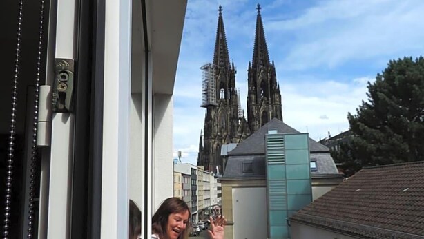 A view of a building with a large window, a person standing by the window, and a cathedral in the background. - Hotel Sandmanns Am Dom (Cologne)