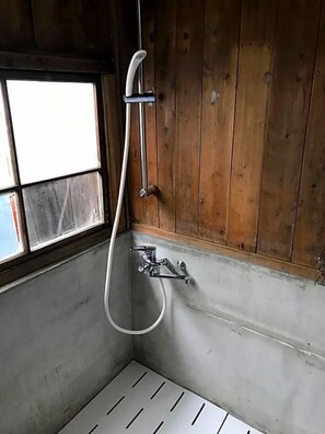 Un baño pequeño con ducha, ventana y paredes de madera.