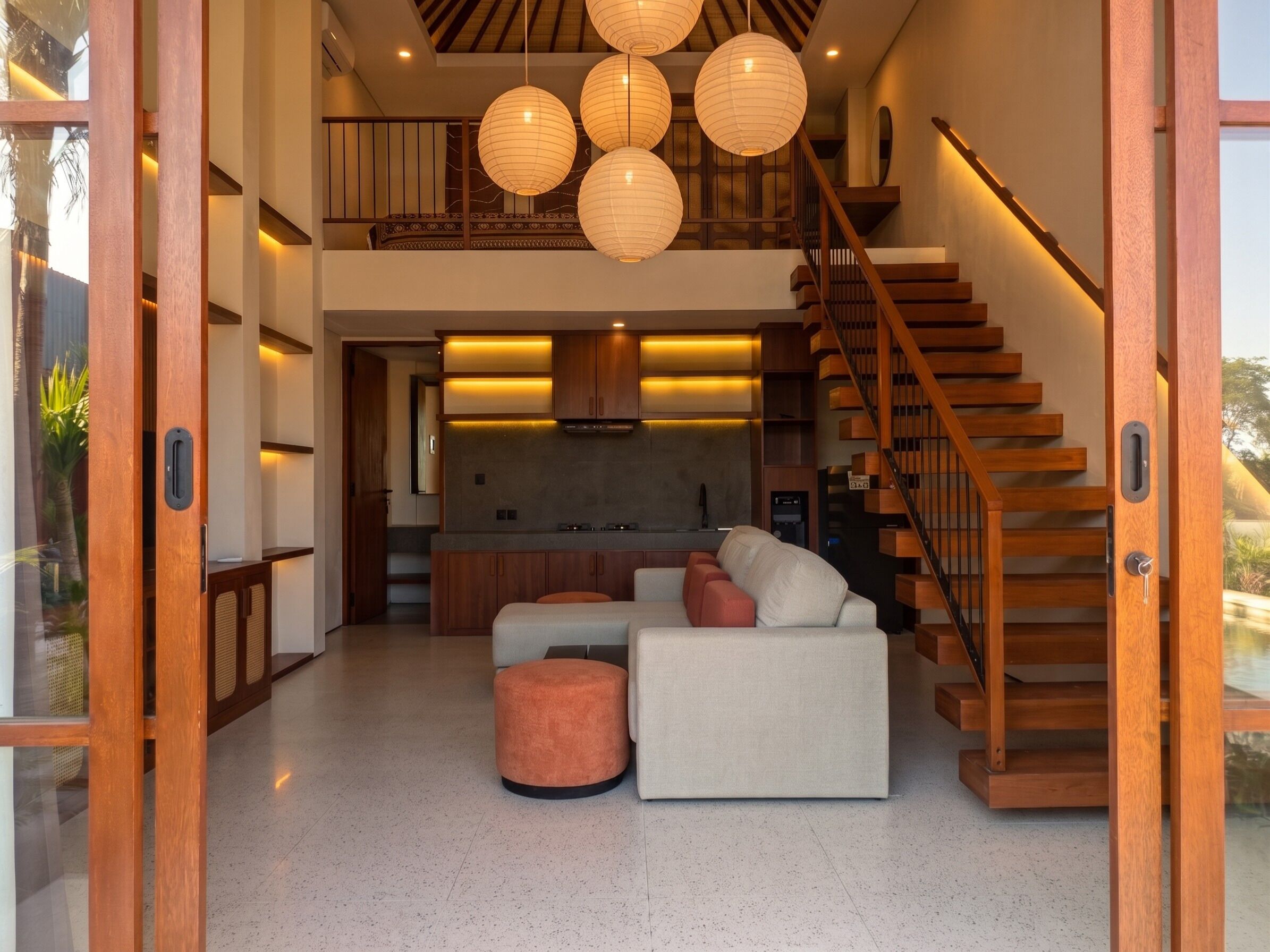 A modern interior with a staircase, wooden flooring, a sofa, and pendant lighting.