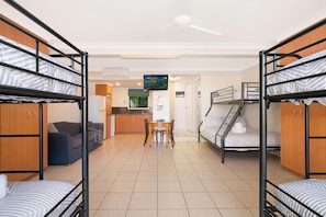 A dormitory room with bunk beds, a kitchenette, a dining area, and a TV.