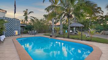 A swimming pool with a tiled deck, surrounded by palm trees and a fence.