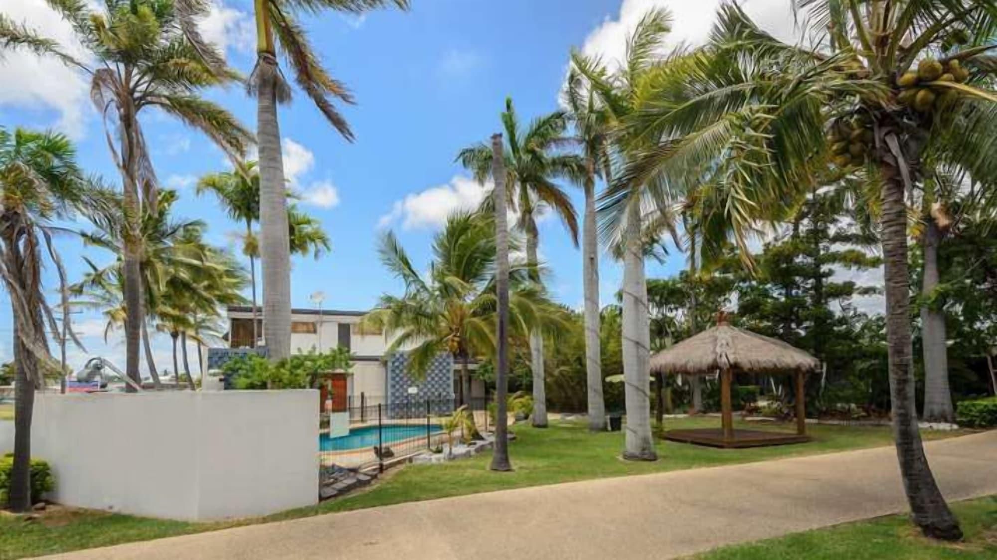 A resort with palm trees, a pool, and a thatched-roof gazebo.