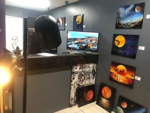 A room with a desk, computer, and various paintings on the wall.