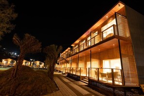 A multi-story hotel with balconies, a covered outdoor seating area, and a pathway leading to the entrance. - Justa Rasa Retreat & Spa Rishikesh (Yamkeshwar)
