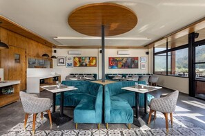 A modern dining area with teal upholstered booths, a central round table, and artwork on the walls. - Justa Rasa Retreat & Spa Rishikesh (Yamkeshwar)