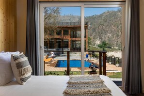 A bedroom with a large bed, a view of a pool, and a mountain landscape. - Justa Rasa Retreat & Spa Rishikesh (Yamkeshwar)