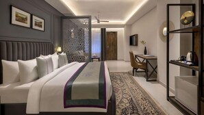 A modern hotel room with a large bed, a desk, a chair, and a television. - Justa Rasa Retreat & Spa Rishikesh (Yamkeshwar)