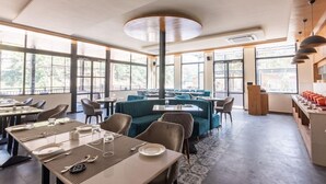 A modern dining area with tables and booths, large windows, and a central column. - Justa Rasa Retreat & Spa Rishikesh (Yamkeshwar)