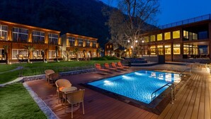 A modern hotel with a swimming pool, outdoor seating, and a view of the surrounding hills. - Justa Rasa Retreat & Spa Rishikesh (Yamkeshwar)