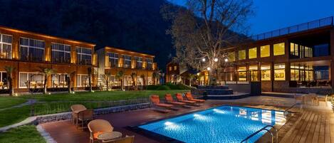 A modern hotel with a swimming pool, outdoor seating, and a view of the surrounding hills.