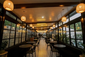 Un restaurant amb una barra llarga, diverses taules i làmpades penjants.