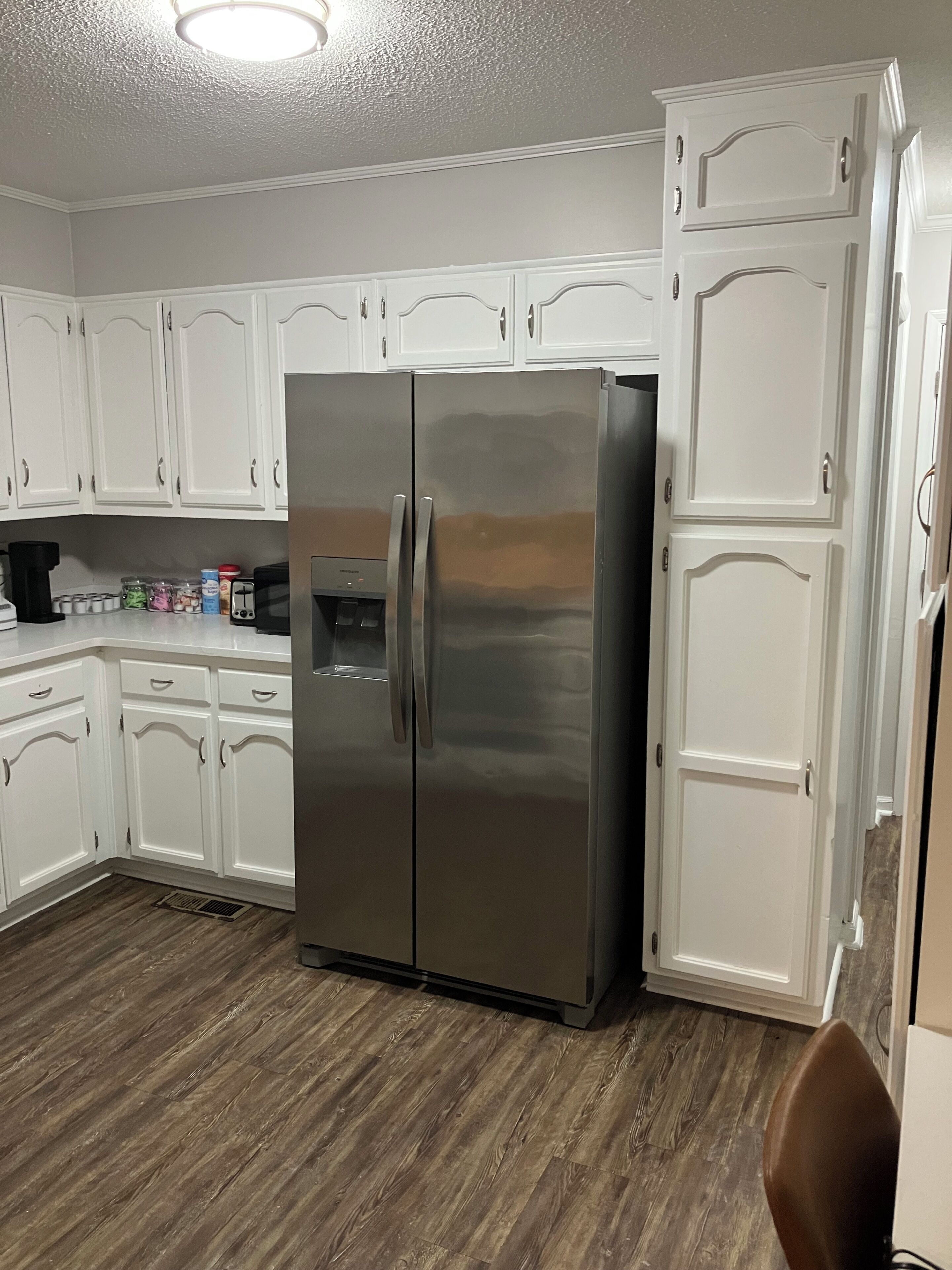 A kitchen with white cabinets, a stainless steel refrigerator, and a coffee maker on the counter.